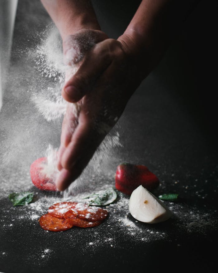 Hands clap flour over fresh vegetables and spices for cooking prep.